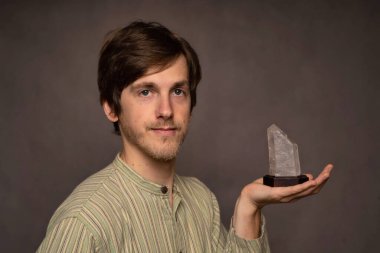 Genç yakışıklı, uzun boylu, zayıf, kahverengi saçlı, kristal görünümlü gri arka planda, çizgili gömlekli, beyaz bir adam.