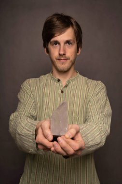 Genç yakışıklı, uzun, zayıf, kahverengi saçlı beyaz adam sana gri arka planda kristal çizgili gömlek teklif ediyor.