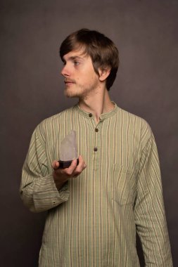 Genç yakışıklı, uzun boylu, zayıf, kahverengi saçlı, kristal rengi, gri arka planda çizgili gömleği olan beyaz bir adam.