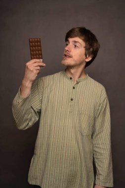 Genç, uzun boylu, zayıf, kahverengi saçlı, gri arka planda çizgili gömlekli, çikolata renkli bir adam.