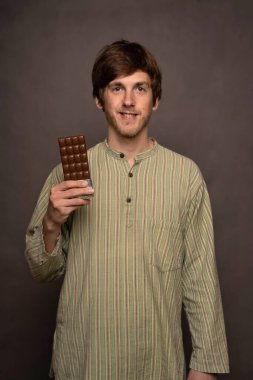 Genç, uzun boylu, zayıf, kahverengi saçlı, sırıtan, gri arka planda çizgili gömlekli, çikolata renkli bir adam.