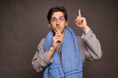 Gri arka planda dişlerini fırçalarken kahverengi saçlı, uzun boylu, zayıf, genç beyaz bir adam fikir üretiyor.