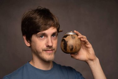 Genç yakışıklı, uzun boylu, zayıf, kahverengi saçlı, mat fincanı ile poz veren gri arka plandaki gri gömlekli adam.