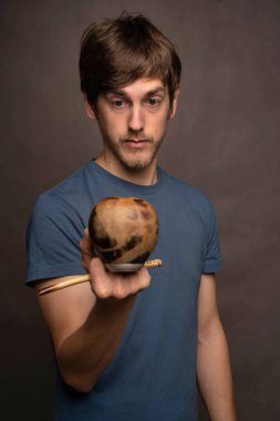 Kahverengi saçlı, uzun boylu, zayıf beyaz bir adam gri arka planda gri gömlekli, kameraya bakan eş fincanı inceliyor.