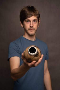 Genç yakışıklı, uzun boylu, zayıf, kahverengi saçlı, gri arka planda gri gömlekli, elinde fincanla kameraya bakan beyaz adam.