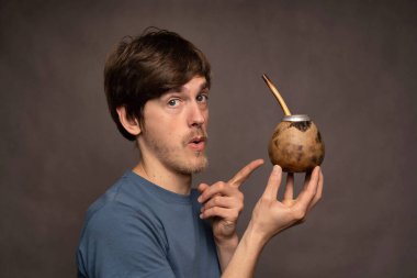 Genç yakışıklı, uzun boylu, zayıf, kahverengi saçlı, gri arka planda fincanı çiftleşmek için gösteren gri gömlekli beyaz adam.