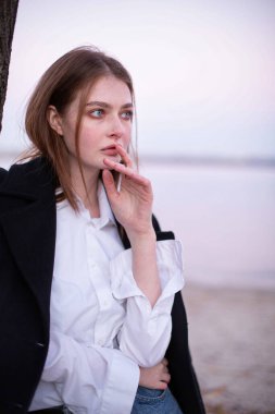 Uzun düz saçlı, koyu renk ceketli, arkasında göl olan beyaz Avrupalı bir kadının portresi.