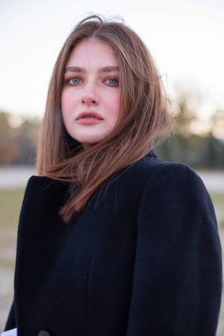 Sonbaharda kumsalda koyu renk ceketli soğuk, düz saçlı, beyaz Avrupalı bir kadının portresi.