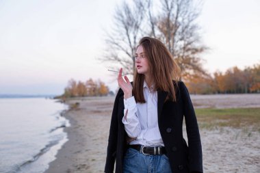 Sonbaharda kumsalda siyah ceketli, uzun düz saçlı, beyaz Avrupalı bir kadın.