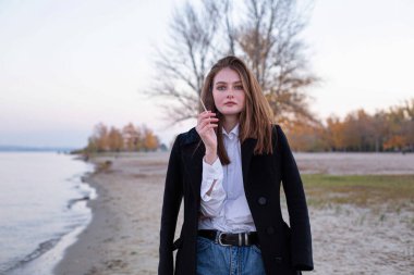 Sonbaharda kumsalda siyah ceketli, uzun düz saçlı, beyaz Avrupalı bir kadın.