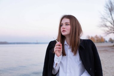 Sonbaharda kumsalda siyah ceketli, uzun düz saçlı, beyaz Avrupalı bir kadın.