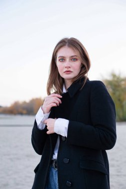 Çekici, uzun düz saçlı, kumsalda sonbaharda koyu renk ceketli beyaz Avrupalı kadın.