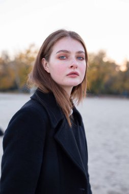 Sonbaharda kumsalda koyu renk ceketli, uzun düz saçlı beyaz Avrupalı bir kadının portresi.