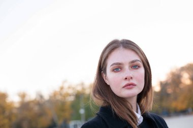 Uzun düz saçlı, beyaz Avrupalı, mavi gözlü, koyu renk ceketli bir kadın.