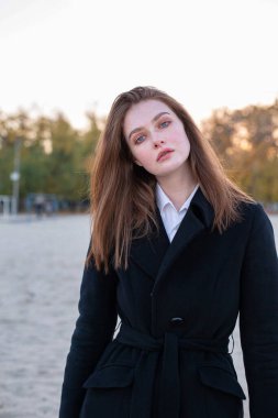 Sonbaharda kumsalda koyu renk ceketli oldukça uzun düz saçlı beyaz Avrupalı bir kadının portresi.