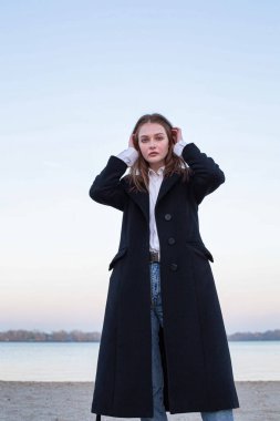 Sonbaharda kumsalda koyu renk ceketli oldukça uzun düz saçlı, beyaz Avrupalı bir kadın.