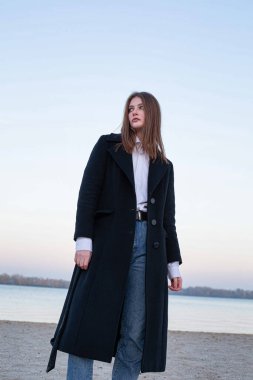 Sonbaharda kumsalda koyu renk ceketli oldukça uzun düz saçlı, beyaz Avrupalı bir kadın.