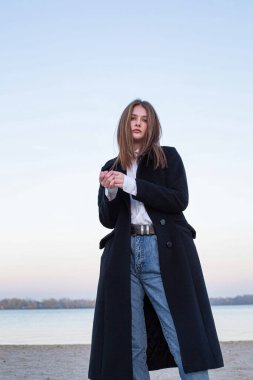 Sonbaharda kumsalda koyu renk ceketli oldukça uzun düz saçlı, beyaz Avrupalı bir kadın.