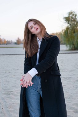 Uzun düz saçlı, beyaz Avrupalı, kumsalda sonbaharda siyah ceketli, beyaz gömlekli bir kadın.