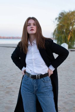 Sonbaharda kumsalda koyu renk ceketli, uzun düz saçlı, beyaz Avrupalı kadın.