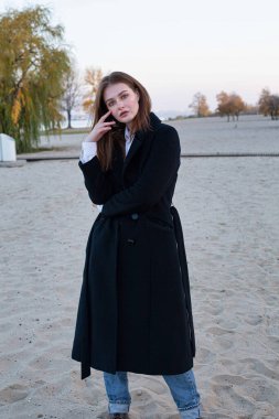 Sonbaharda kumsalda yüzü koyu renk ceketli, uzun düz saçlı, beyaz Avrupalı kadın.