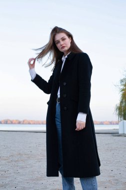 Sonbaharda kumsalda siyah ceketli, uzun düz saçlı, beyaz Avrupalı kadın.