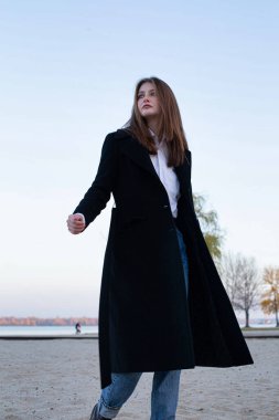 Sonbaharda kumsalda uzun düz saçlı, koyu renk ceketli beyaz Avrupalı bir kadın.