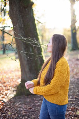 Güneşli sonbahar ormanlarında, sarı kazaklı, Avrupalı beyaz bir kadın.