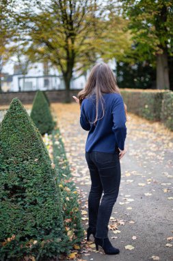 Sonbahar parkında koyu mavi kazaklı genç Avrupalı bir kadın geri döndü.