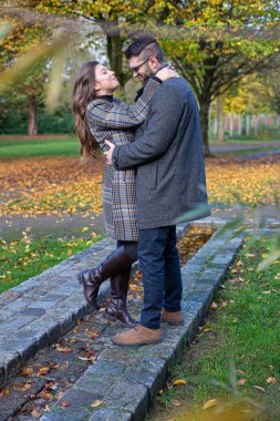 Sonbahar parkında siyah saçlı beyaz Avrupalı kadın ve erkeği kucaklarken mutlu ol.