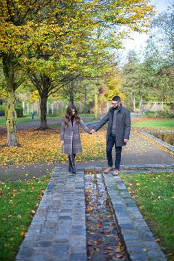 Sonbahar parkında el ele tutuşan beyaz adam ve kadın.