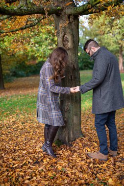 Ormanda sarı yapraklı beyaz adam ve kadını seyrediyor.
