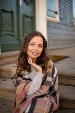 Eski bir binanın yanındaki atkıya sarılı kıvırcık saçlı genç bir kadının portresi.