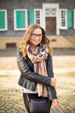 Güzel gülümseyen beyaz Avrupalı, kahverengi saçlı, sonbaharda bina arkasında.