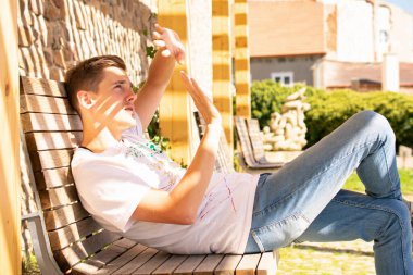 Beyaz kotlu kahverengi saçlı yakışıklı beyaz adam şehir parkında güneşten yüzünü kapatıyor.