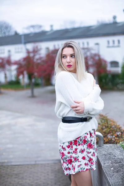 在一个城市 寒冷的年轻的欧洲白人妇女 穿着白色毛衣 穿着花裙子 头发金黄 — 图库照片