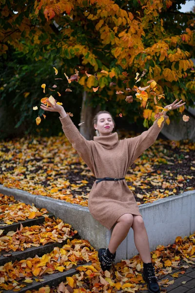 Sarışın, sarı yapraklı, beyaz Avrupalı bir kadın yaprakları fırlatıyor.
