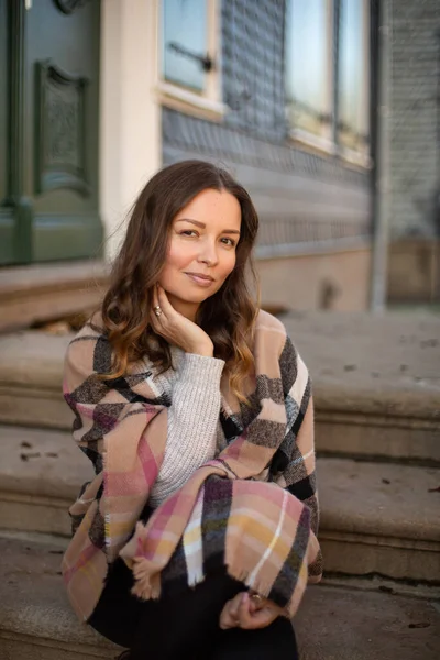 Eski bir binanın yanındaki atkıya sarılı kıvırcık saçlı genç bir kadının portresi.