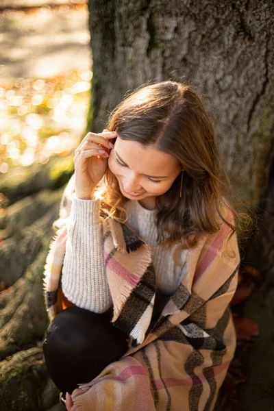 Genç Avrupalı beyaz kadın, kahverengi saçlı, ağacın yanında sıcak bir sonbahar eşarbı var.