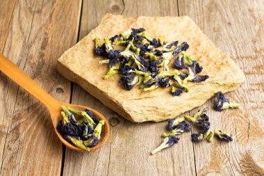 Tahta bir kaşıkta bir sürü kuru klitorya ve eski ahşap üzerinde doğal düz kaya var.