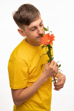 Genç, uzun boylu, zayıf, kahverengi saçlı, turuncu çiçekli, sarı gömlekli beyaz bir adam.