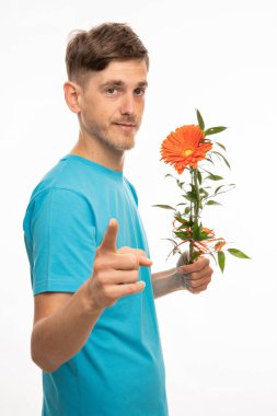 Genç, uzun boylu, zayıf, kahverengi saçlı, turuncu çiçekli, beyaz arka planda izole edilmiş mavi gömlekli bir adam.