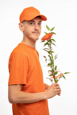 Genç yakışıklı, uzun boylu, zayıf, kahverengi saçlı, turuncu çiçekli beyaz adam beyaz arka planda izole edilmiş turuncu gömlekli kameraya bakıyor.