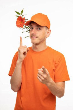 Genç, uzun boylu, zayıf, kahverengi saçlı, turuncu çiçekli, beyaz arka planda turuncu gömlekli genç bir adam.