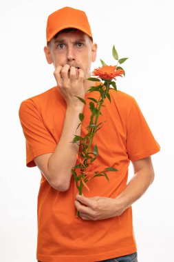 Yakışıklı, uzun boylu, zayıf, kahverengi saçlı, turuncu çiçekli, turuncu gömlekli, beyaz arka planda turuncu şapkalı, gergin bir adam.