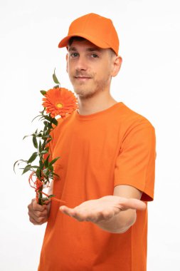 Yakışıklı, uzun boylu, zayıf, kahverengi saçlı, elinde turuncu çiçekle beyaz arka planda izole edilmiş turuncu gömlekli bir adam.