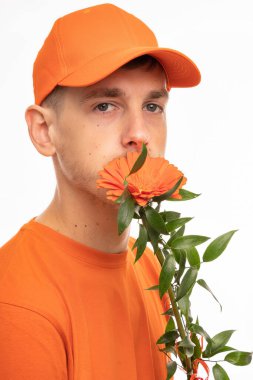 Yakışıklı, uzun boylu, zayıf, kahverengi saçlı, turuncu çiçekli, turuncu gömlekli ve beyaz arka planda izole edilmiş turuncu şapkalı genç adam.