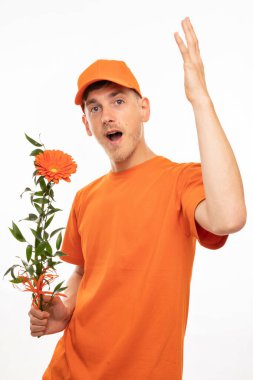 Genç, uzun boylu, zayıf, kahverengi saçlı, turuncu çiçekli, turuncu gömlekli ve beyaz arka planda izole edilmiş turuncu şapkalı genç adam.