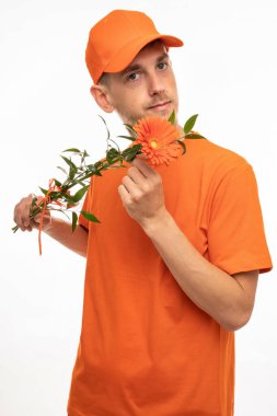 Yakışıklı, uzun boylu, zayıf, kahverengi saçlı, turuncu çiçekli, beyaz arka planda turuncu gömlekli genç bir adam.