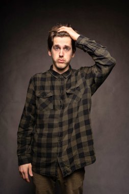 Genç, uzun boylu, zayıf, kahverengi saçlı, gri arka planda flanel gömlekli, yakışıklı, beyaz bir adam.